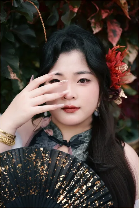 身穿墨色印花旗袍的女子以手掩面，手持洒金黑扇，身后是红叶