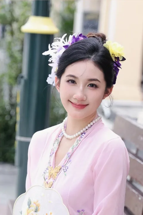身穿粉色可峇雅、戴珍珠颈链的女子，背后是洒满阳光的老街
