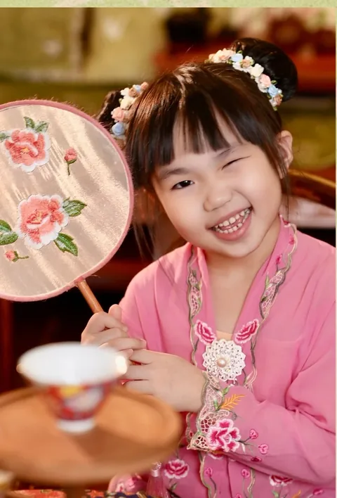 身穿粉色可峇雅的女孩手持牡丹团扇开怀大笑