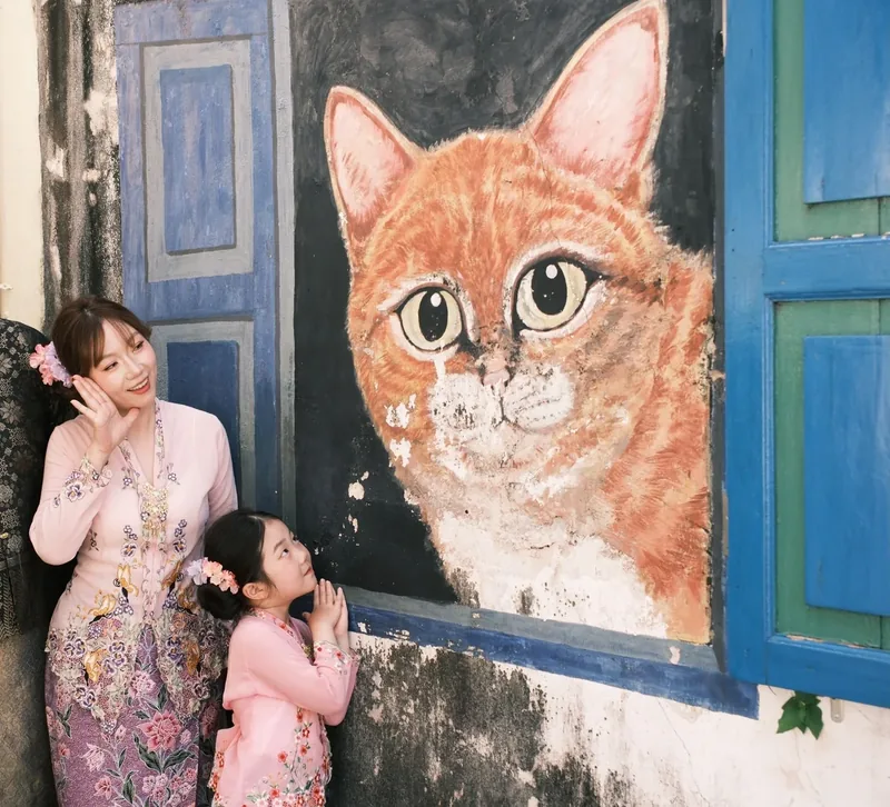 母女穿着娘惹衫，在乔治市巨型花猫壁画前合影