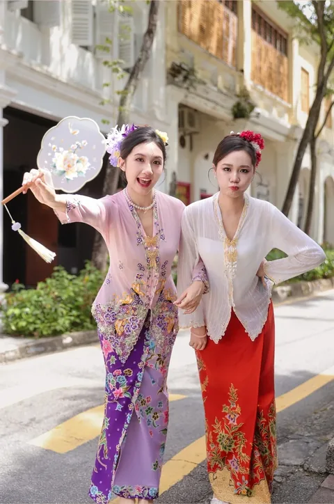 两位年轻女子分别身穿粉色与白色可峇雅，在店屋老街上嬉笑
